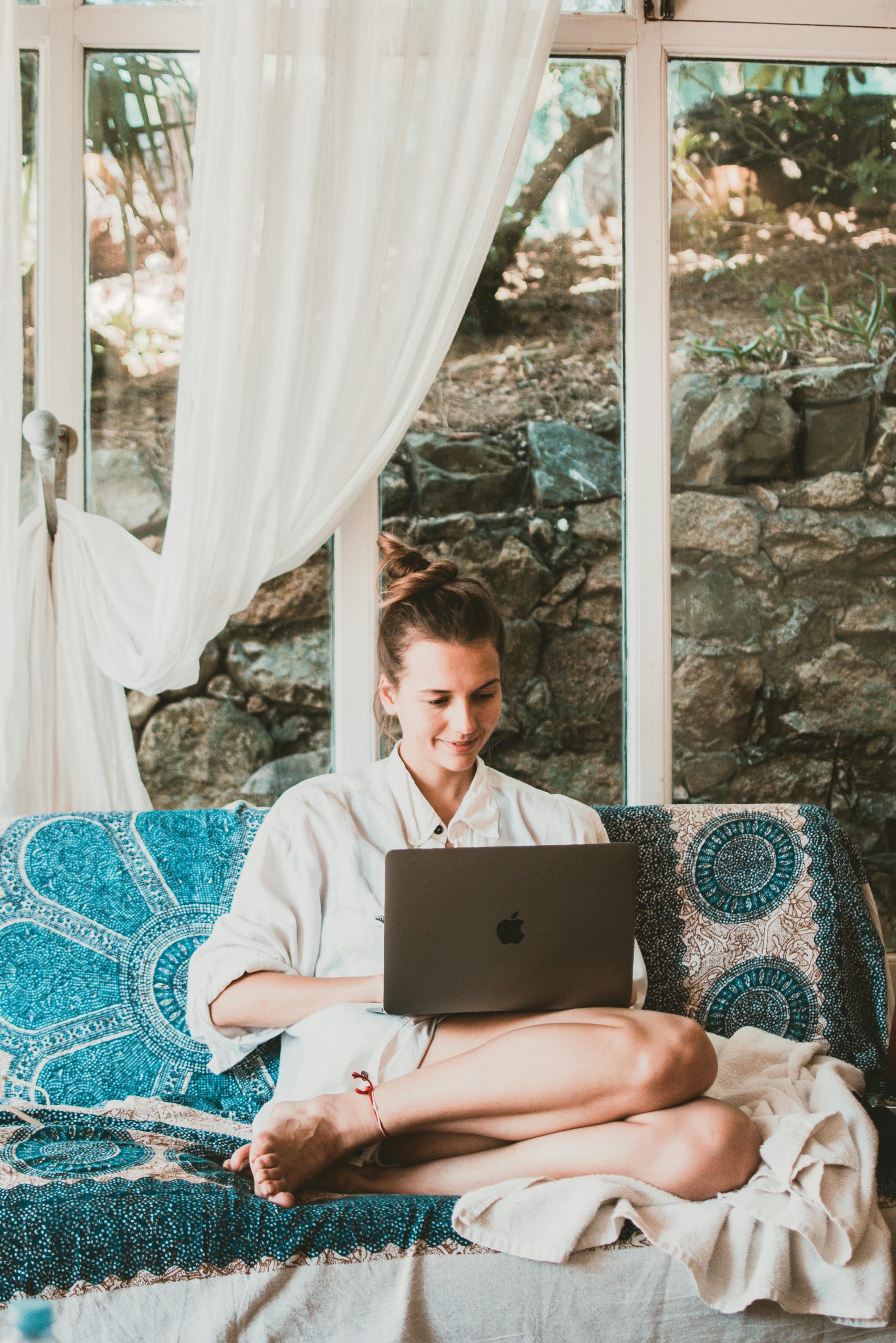 A woman sitting comfortably on a sofa using a laptop, depicting a serene remote work setup.